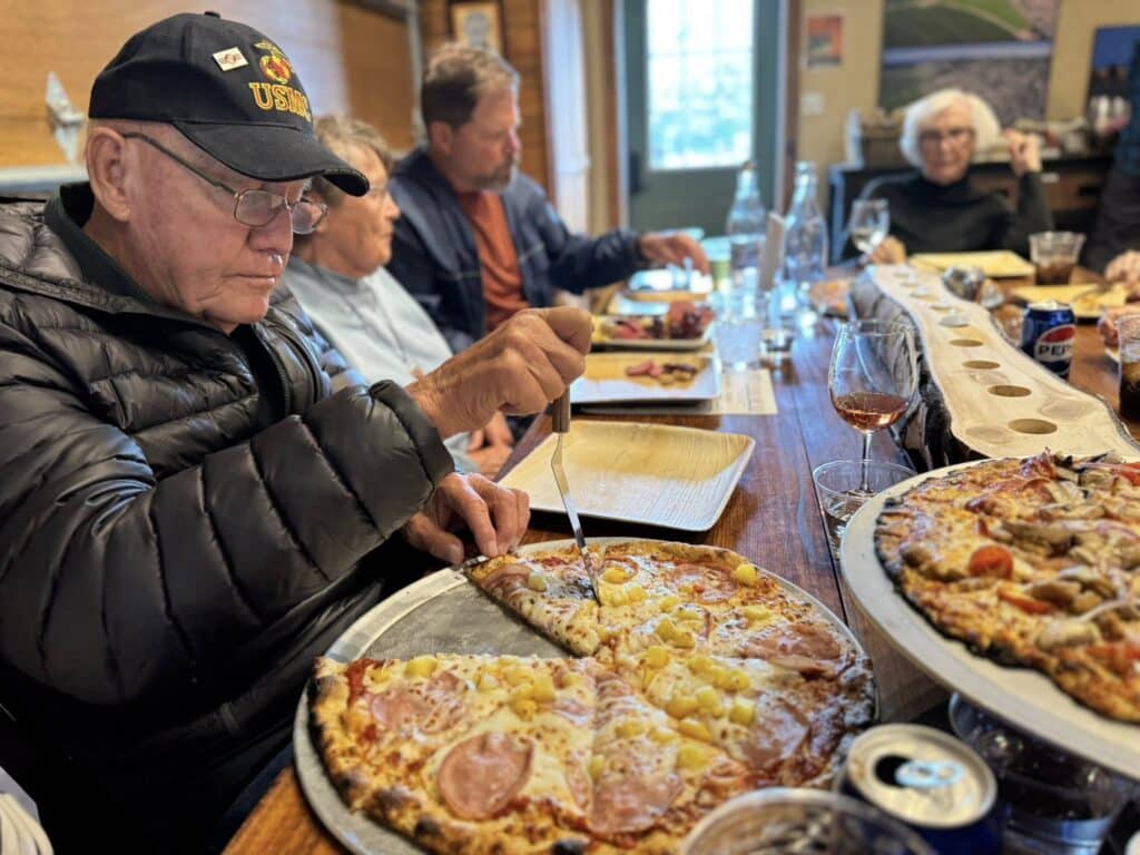 Residents at The Lodge Retirement Community in Sisters, Oregon enjoying a meal together, sharing pizza and conversation around the dining table.